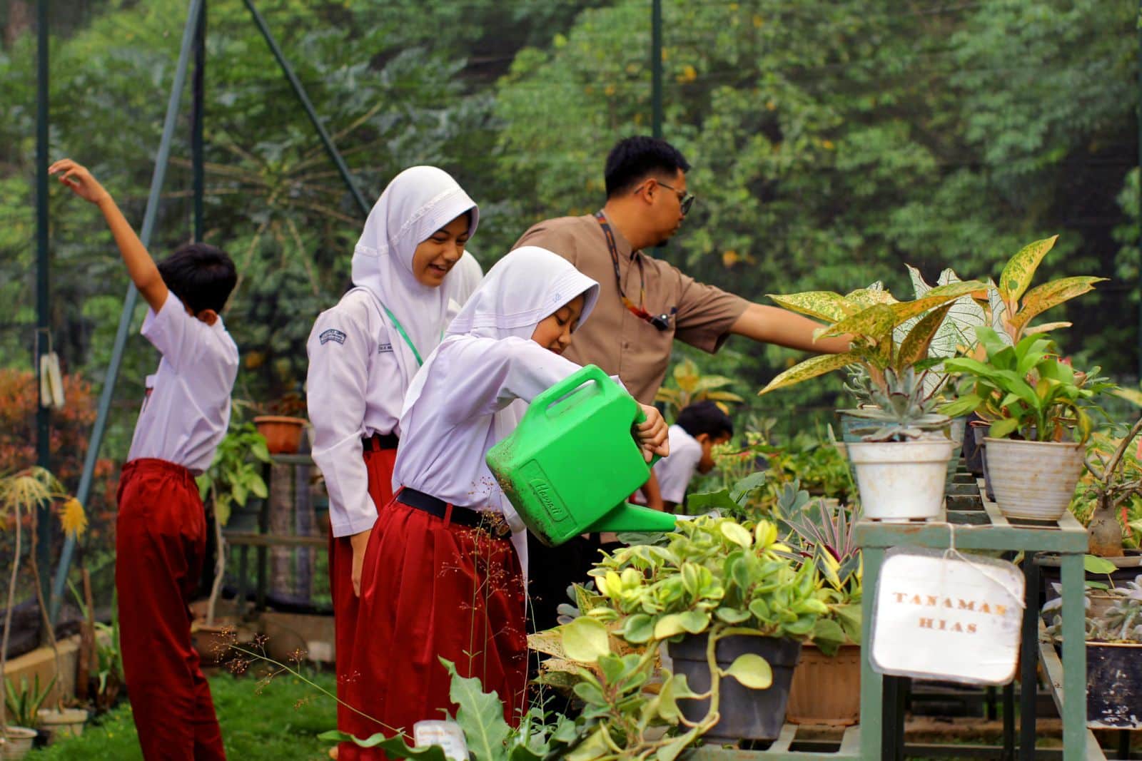 A student in a hijab waters plants with a green watering can as her classmate and a male teacher look on, during the Green Guardians climate education program
