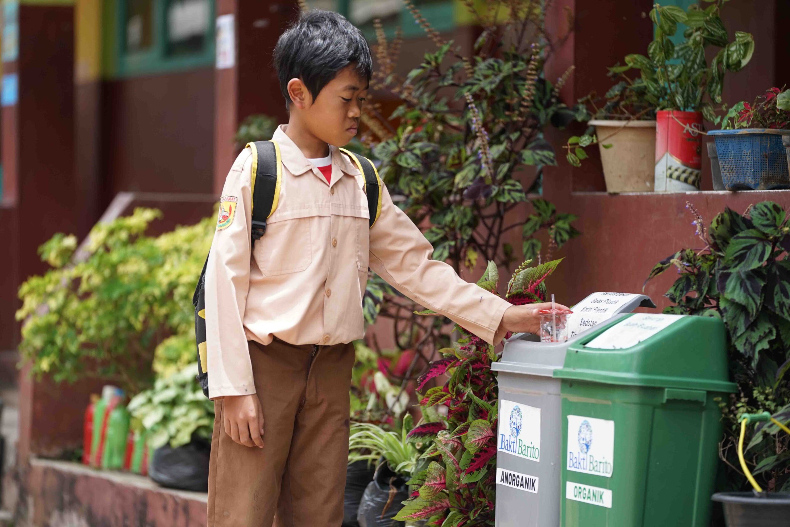 A student practices waste separation as part of the Green Guardians climate education program by Bakti Barito, placing a plastic cup into the designated inorganic trash bin at his school.