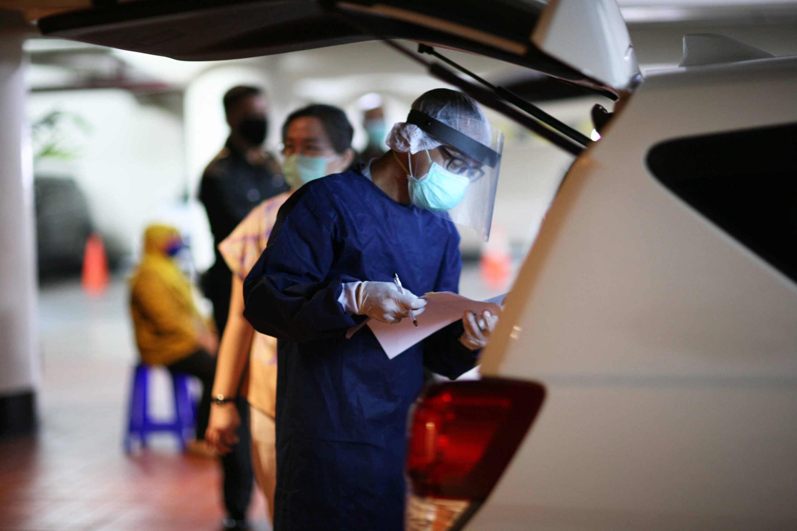 A healthcare worker in full PPE manages logistics for COVID-19 testing, illustrating the pandemic response efforts supported by the Barito Pacific Group's contribution.