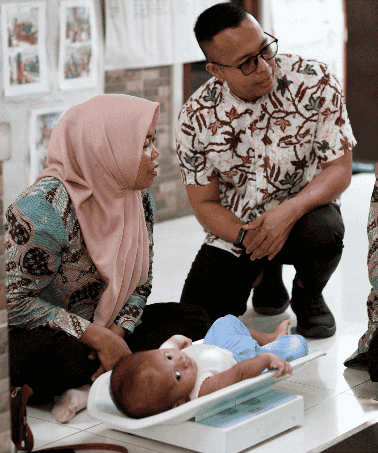 At a Bakti Barito community health event for stunting prevention, a male program manager of bakti barito in a batik shirt and a female health worker in a hijab monitor the weight of a baby on a portable infant scale