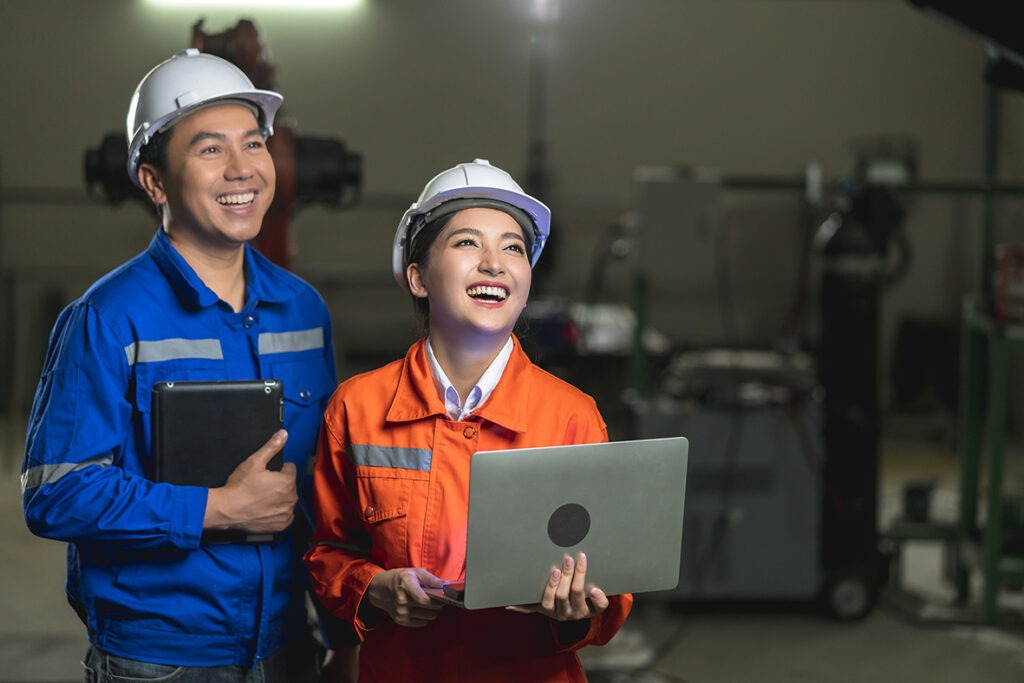 Two industrial professionals in safety gear collaborating with a laptop and tablet in a workshop setting.