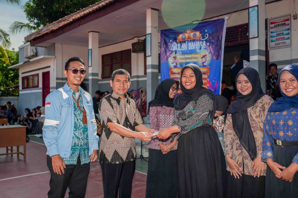 Company representatives presenting an award or scholarship certificate to a student during a 'Bulan Bahasa' (Language Month) event at a school.